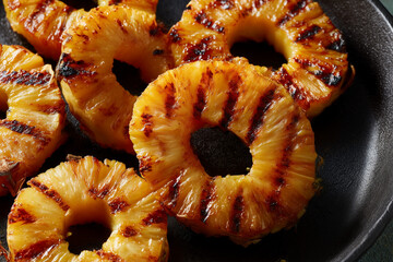 Grilled pineapple slices served on a black plate, showcasing caramelization and grill marks