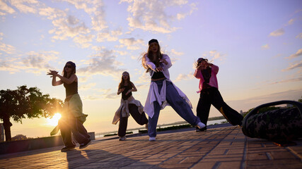 Motion power. Group of young, diverse dancers performs energetically on an urban street at sunset....