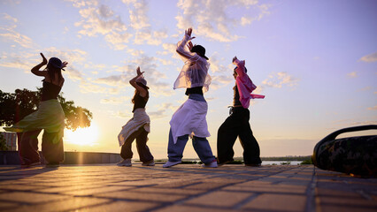 Street dancers are silhouetted against a vibrant sunset sky, performing energetic moves on an urban...