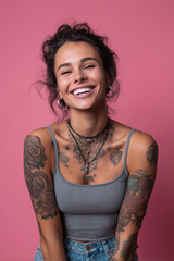 Smiling woman with tattoos against a pink backdrop showcasing joy and confidence in a cozy indoor setting