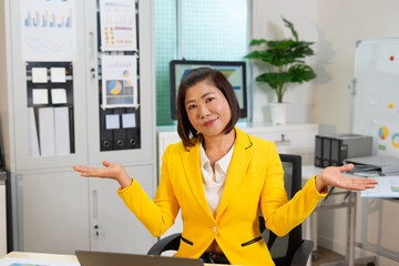 Confident businesswoman in yellow jacket smiling with open hands in modern office space