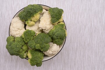 Fresh broccoli and cauliflower in bowl on fabric surface