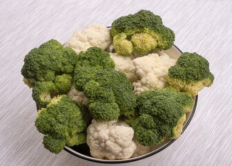 Fresh broccoli and cauliflower in bowl on fabric surface