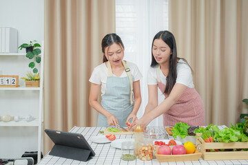 Asian young two women cooking salad in kitchen. Active beautiful girl feel happy and enjoy eating vegetables healthy foods to diet and lose weight for health care in house	