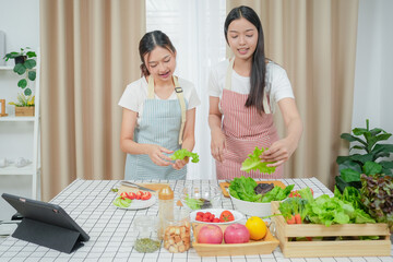 Asian young two women cooking salad in kitchen. Active beautiful girl feel happy and enjoy eating vegetables healthy foods to diet and lose weight for health care in house	