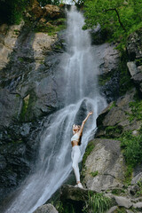 woman stretching near waterfall, outdoor fitness activity, natural green environment, healthy lifestyle, athletic yoga pose, serene mountain setting