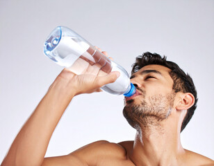 Un hombre joven bebiendo de una botella de agua para la sed e hidratarse durante una ola de calor con altas temperaturas en verano con fondo blanco