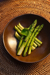 Grilled asparagus spears artfully arranged in a rustic brown bowl, with a single leaf.