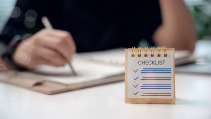 Close-up of a checklist on a desk with a businessman writing in a notebook, representing planning, productivity, and task management.