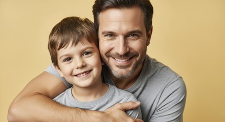 A proud father and his young son smiling cheerfully, sharing a strong embrace on a yellow background.