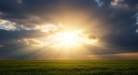Obraz premium Sunlight breaking through the clouds over a green field.
