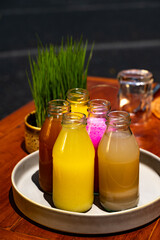 Colorful juices in glass bottles on a wooden table, with wheatgrass.