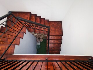 Top view of indoor wooden staircase with dark parquet and black iron railing, showing spiral layout, depth, and architectural design in residential space.