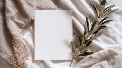 Elegant wedding stationery flat lay mockup with a blank vertical card and an olive branch atop soft white linen