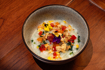 Creamy rice dish garnished with colorful vegetables, nuts, and edible flowers, served in a rustic bowl.