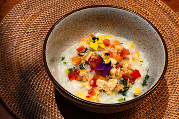 A bowl of creamy rice dish, garnished with colorful flowers and vegetables.