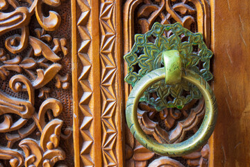 Close-up of old brass hanging ring door knob covered with patina with floral ornament on carved wooden door