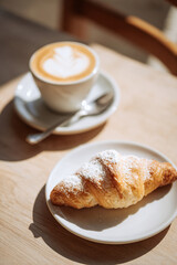 Cornetto pastry rests beside a creamy cappuccino in a white ceramic cup