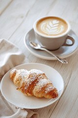 Cornetto pastry rests beside a creamy cappuccino in a white ceramic cup