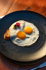 Fried eggs with toast and garnish on a dark plate, breakfast meal.