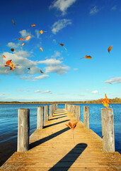 Tranquil Autumn Lake with a Wooden Pier and Dancing Colorful Leaves in Warm Sunlight