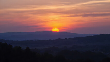 Obraz premium Warm Hues Paint The Sky As The Sun Dips Below The Mountain Range At Dusk Creating A Peaceful Mood