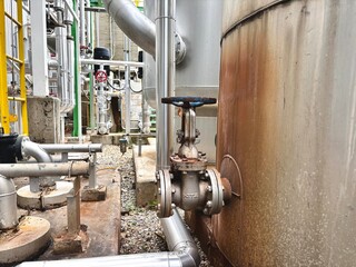 Industrial valve connected to a large storage tank with stainless steel piping in a factory setting. Commonly used in chemical plants, refineries, or water treatment system