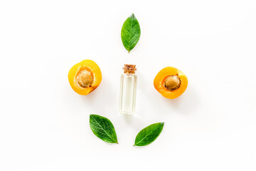 Apricot kernel oil among apricots and leaves on white background top view pattern