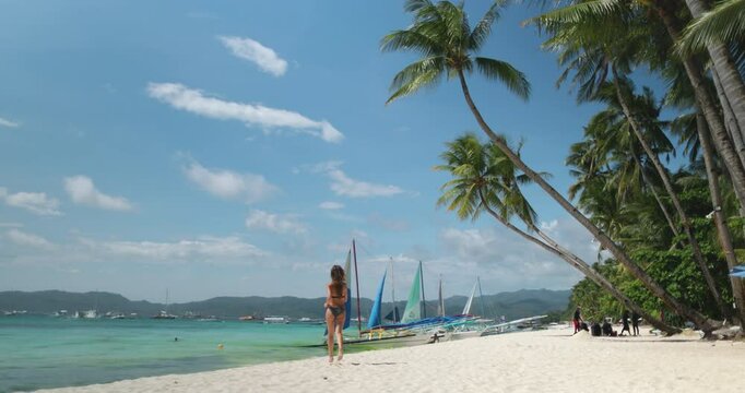 Woman joyfully runs on a white beach in boracay, philippines, surrounded by traditional sailboats and clear turquoise waters, creating a serene and exotic vacation scene