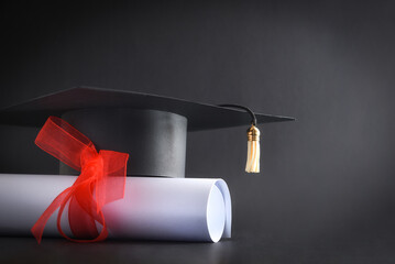 Academic cap and diploma with red ribbon isolated on black