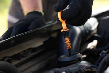 Worker checking motor oil level in car with dipstick, closeup