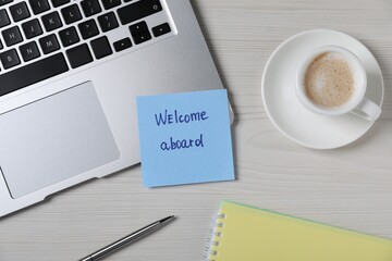 Paper note with word Welcome Aboard, laptop, cup of coffee and pen on light wooden table, flat lay