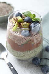 Delicious chocolate pudding with chia seeds, kiwi, mint and blueberries in glass on grey table, closeup