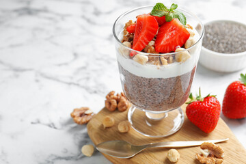 Delicious chocolate pudding with chia seeds, strawberries, yogurt and nuts in glass on white marble table, closeup. Space for text
