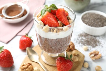 Delicious chocolate pudding with chia seeds, strawberries, yogurt and nuts in glass on white marble table, closeup