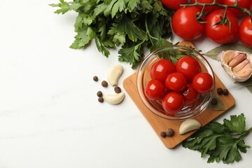 Tasty pickled tomatoes, parsley and spices on white table, flat lay. Space for text