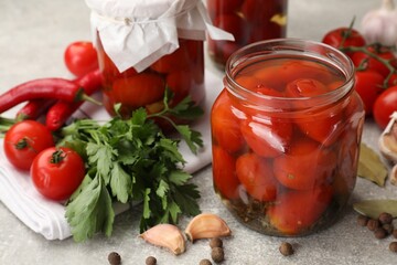 Tasty pickled tomatoes in jars, products and spices on grey textured table, closeup