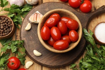 Tasty pickled tomatoes in bowl and ingredients on wooden table, flat lay
