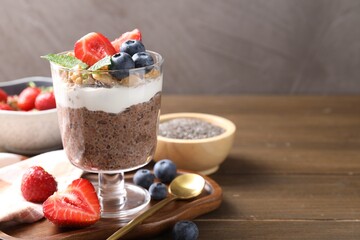 Delicious chocolate pudding with chia seeds, nuts and berries in glass on wooden table, closeup....