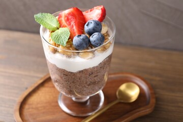 Delicious chocolate pudding with chia seeds, nuts and berries in glass on wooden table, closeup