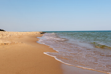 A pristine, empty sandy beach stretches along the coastline with gentle waves washing ashore under...