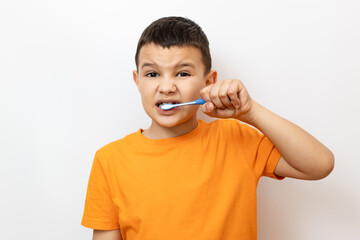 A little boy in an orange T-shirt carefully brushes his teeth.