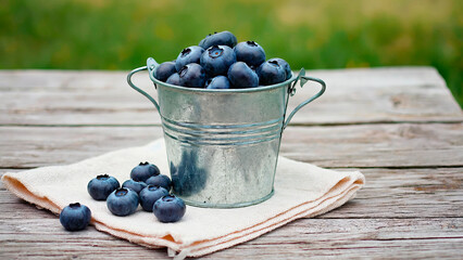 Metal bucket filled with blueberries stands on light napkin on wooden surface. Calm summer background.