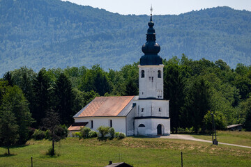 Rustic countryside church featuring white walls and distinctive black baroque spire, surrounded by...