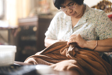 Asian elderly woman using sewing needle repair blanket Older people stay at home