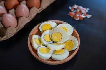A pile of halved hard boiled eggs in a wooden bowl with a few whole eggs on top of the egg carpet...