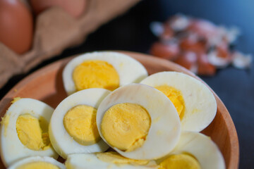 Closeup, A pile of halved hard boiled eggs in a wooden bowl with a few whole eggs on top of the egg carpet and egg shells