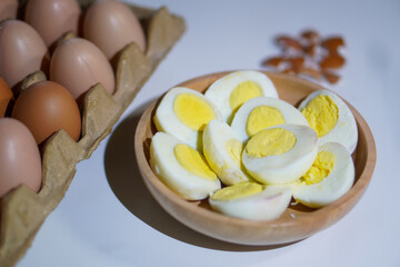 A pile of halved hard boiled eggs in a wooden bowl with a few whole eggs on top of the egg carpet and egg shells