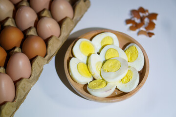 A pile of halved hard boiled eggs in a wooden bowl with a few whole eggs on top of the egg carpet and egg shells