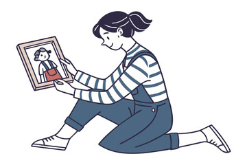 A young girl in overalls and striped shirt sits on the floor happily looking at a framed photograph of a child